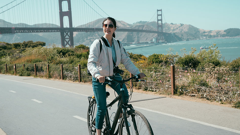 A person on a bicycle with a bridge in the background.