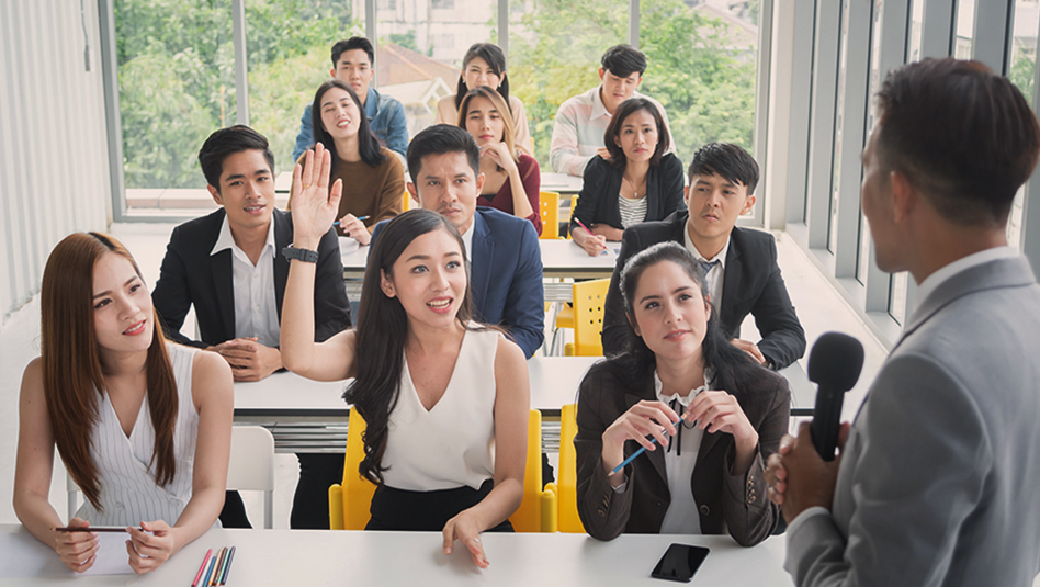 A group of young professionals in office attire listening to a speaker in front of them.