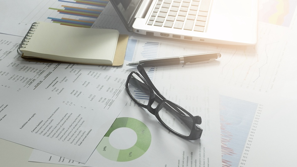 Notebook, laptop, pen, glasses, and printed charts on a table